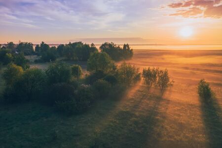 Magnificent dawn with the sun in the fog over the field and forest. Morning summer landscape of Belarusの写真素材