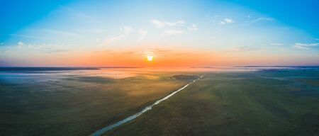 A magnificent panorama of the Belarusian field in the morning at dawn with fog and a river. Beautiful sun goes out of the horizon. Aerial viewの写真素材