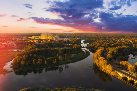 Breathtaking Aerial View Showcasing Beautiful Rivers Surrounded by a Stunning Sunset Landscape. A paper factory on the bank of the riverの写真素材