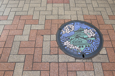 Osaka, Japan - April 25, 2016: A manhole cover in Osaka, Japan. The Osaka castle and sakura engraved on to a manhole cover as a symbol of an important city's landmarkのeditorial素材