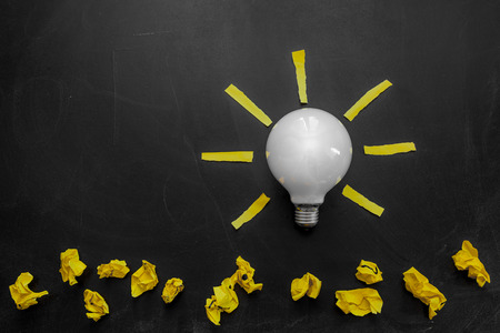 Light bulb with rays made from yellow stickers on the black chalkboard   and crumpled papers, light bulb idea , business idea , business concept ,Innovation conceptの写真素材