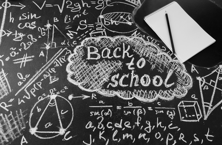 Back to school background with title "Back to school",  formulas written by white chalk on the black school chalkboard and notebook with pencilの写真素材
