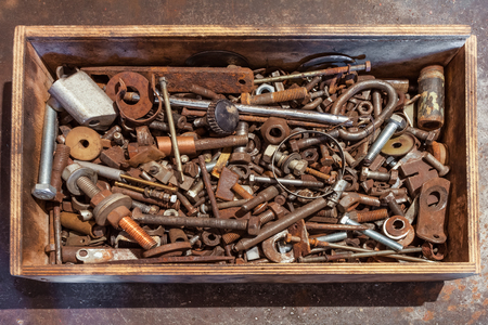 Wooden box with bolts, screws, nuts, bearings, valves, washers, nails on the metal background