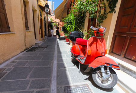 Rethymnon, Island Crete, Greece, - July 1, 2016: A red old parked scooter and a local citizen in the end of the narrow street of the old town's part of city Rethymnonのeditorial素材