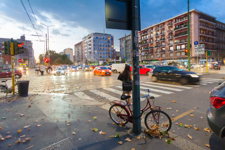 MILAN, ITALY - September 06, 2016: Red colored bicycle parked (fastened by lock) to the street pole lighting on the street of Milan on the evening and blurred cars' moving on the street.のeditorial素材