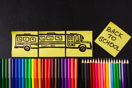 Back to school background with a lot of colorful felt-tip pens and colorful pencils, titles "Back to school" and drawing of school bus drawn on the yellow pieces of paper on the black school chalkboardの写真素材
