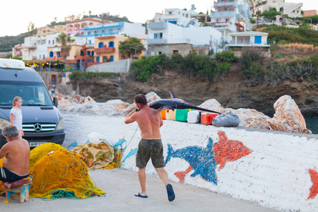 Bali, Island Crete, Greece, - June 30, 2016: Man is a fisherman carries a big fish (sawfish) after successful fish catch from the fishing boat.のeditorial素材