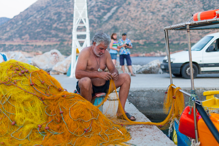 Bali, Island Crete, Greece, - June 30, 2016: Elderly fisherman are repairing the fish net near fishing boat on the pier located on Crete island in Greece.のeditorial素材