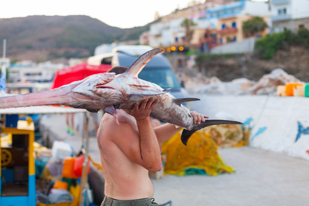 Bali, Island Crete, Greece, - June 30, 2016: Man is a fisherman carries a big fish (sawfish) after successful fish catch from the fishing boat.のeditorial素材