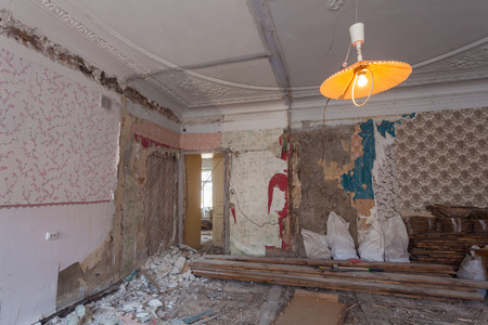 View the vintage room with fretwork on the ceiling of the apartment during under renovation, remodeling and construction.Garbage of constraction materials and lamp in dark room during of disassembling floors and walls.の写真素材