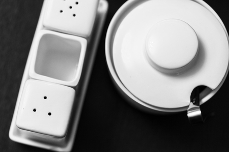 Black and white image of salt and pepper shakers, sugar-bowl and paper napkin holder in the wooden tableの写真素材