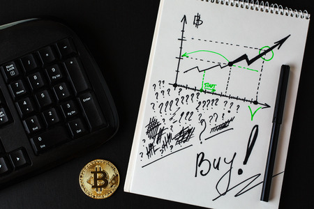 Gold bitcoin, part of  keyboard and ring-bound notebook with diagram with increasing of digital currency of bitcoin and title "Buy !" and  question marks are  written by black marker. Concept of Thinking and writting on the paper to buy or not to buy bitcoins.の写真素材