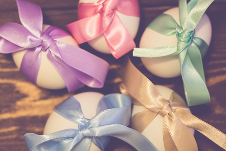 Easter eggs are tied in bows of color ribbons on the wooden background with tone effectの写真素材