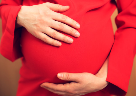 Pregnant woman in red dress is holding belly by hands. Young woman is expecting a baby.の写真素材