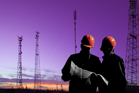 Silhouette of professional industrial climber in helmet and uniform works at height for instaling communication equipment and antenna and telecommunication towers with sunset sky as background. Risky extreme job. Industrial climbing.Industrial climbing background at construction site.の写真素材