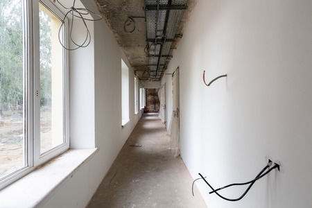 Long and narrow corridor with windows, doors, cable trays and walls with not installed electrical...
