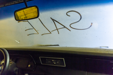 Inside  view of old broken car interior with dusty vehicle dashboard, back mirror, driving steering wheel and dirty wind screen with title SALE written outside. Concept of sale pre-owne cars.の写真素材