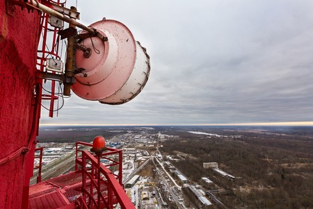 High red chimney of power plant with outdoor telecommunication high capacity microwave gear and huge radio antenna in cloudy day. Powerhouse with river as a backgroundの写真素材