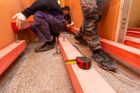Tape-measure on the wooden block and blurred background with  construction workers who working in apartment that is under construction, remodeling, renovation, overhaul, extension, restoration and reconstruction. Concept of total home improvementの写真素材