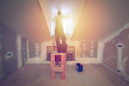 Worker is installing pvc window from wooden platform in small romm of  apartment that is under construction, remodeling, renovation, overhaul, extension, restoration and reconstruction. Concept of home improvement.の写真素材