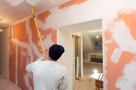 Worker is painting the ceiling by paint roller in corridor  an apartment is inder construction, remodeling, renovation, overhaul, extension, restoration and reconstruction. Concept of home improvement or renovate.の写真素材