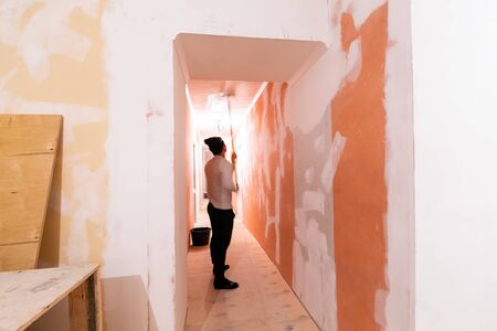 Worker is painting the ceiling by paint roller in corridor  an apartment is inder construction, remodeling, renovation, overhaul, extension, restoration and reconstruction. Concept of home improvement or renovate.の写真素材