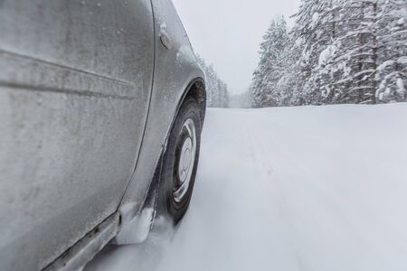 View focused on the car tire during in motion on snowy rural road during snowfall.の写真素材