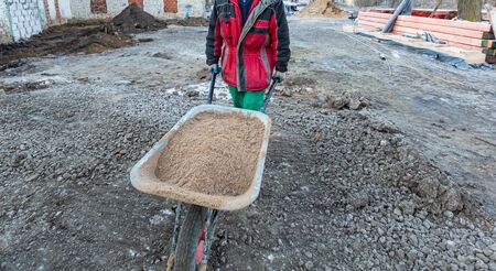 Worker in protect gloves is hauling the building trolley with sand to making the concrete in...