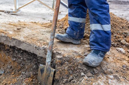 Worker in dirty uniform and shoes with shovel is digging a pit on construction site. Concept of hard...