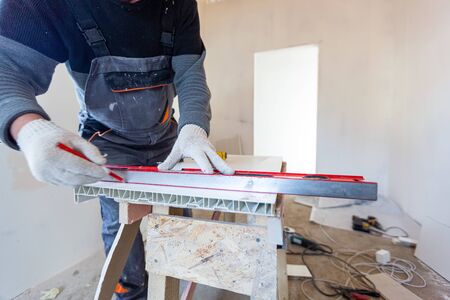 Worker is measuring the plastic detail before it cutting in apartment that is under construction,...