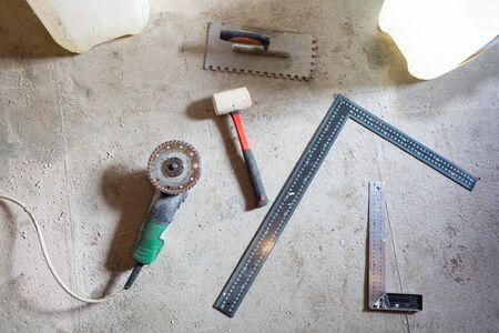Cement floor with tools - angle grinder, construction rulers and humer are in the apartment that is under construction, remodeling, renovation, overhaul, extension, restoration and reconstruction. Concept of home improvement.の写真素材