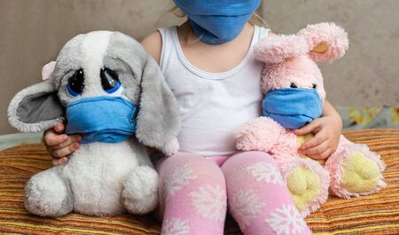 Masked child - protection against influenza virus. Little Caucasian girl wearing mask for protect and her toys with mask are staying in home. Concept of epidemic and pandemic.の写真素材