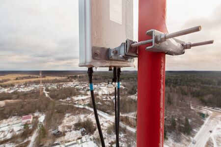 Top of red telecommunication tower with vertical panel antenna and remote radio unit, power and...