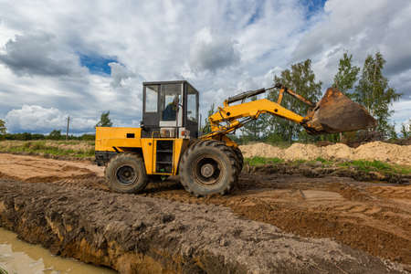 Road Construction and one of the construction machinery - bulldozer is flattenings the sand on the...