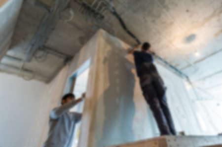 Workers in bokeh. Men are installing the electrical wires on the ceiling in apartment is under construction, remodeling, renovation, extension, restoration and reconstruction. Concept of home improvement and renovationの写真素材