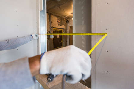 Worker measures distance in doorway after installing drywall in apartment that is under constructionの写真素材