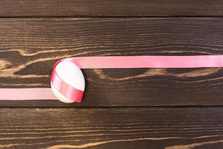 Easter egg is tied pink ribbon on the wooden backgroundの写真素材