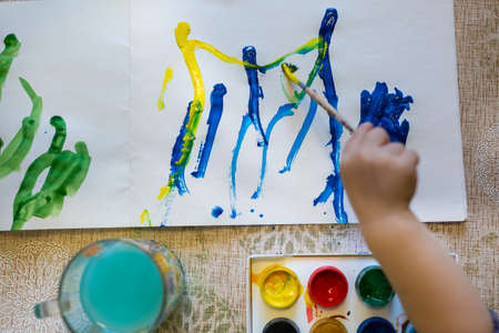 Top view of the small child is drawing with bright paints on paper, close up.の写真素材