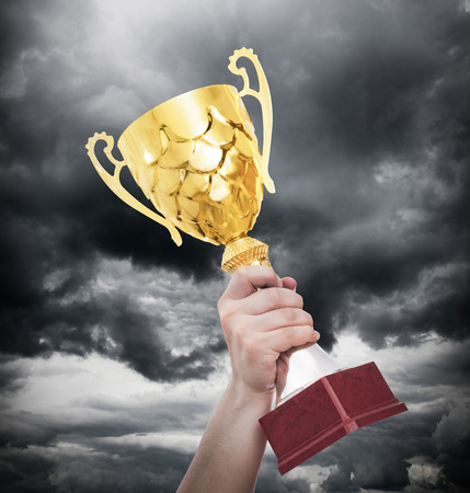 Hands squeeze the cup winner against lightning dark sky.の写真素材