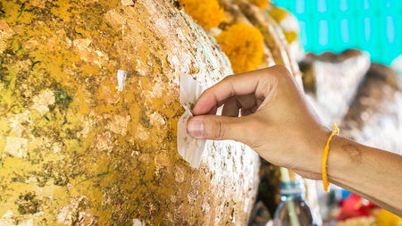 Selective focus of people hand put the gold leaf gilding on Posture of the Buddha.の写真素材