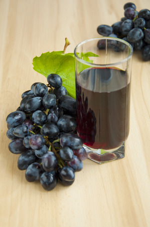 Glass of grape juice on a table with red grapes on wooden backgroundの写真素材