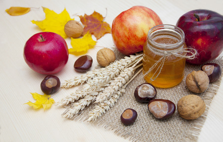 Glass jar of honey with apples, ears of wheat, chestnuts and walnuts on a wooden backgroundの写真素材