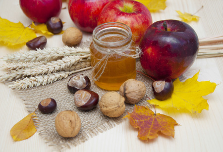 Glass jar of honey with apples, ears of wheat, chestnuts and walnuts on a wooden の写真素材