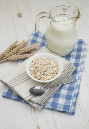 Rolled oats in a white bowl on a napkin with spoon and milk on a wooden backgroundの写真素材