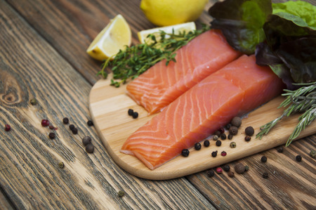 Portion of fresh salmon fillet with aromatic spices and herbs on a wooden backgroundの写真素材