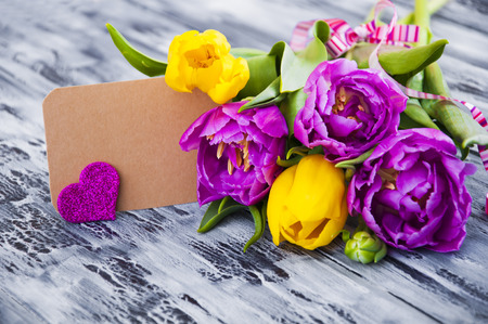Beautiful purple and yellow tulips  with a card on wooden backgroundの写真素材