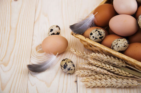 Different types of eggs in a basket with wheat on wooden backgroundの写真素材