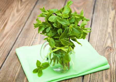 Fresh mint in a vase on a napkin on old wooden background