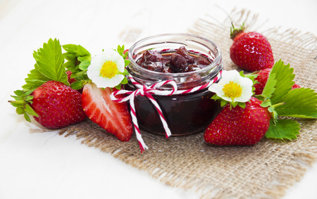 Fresh strawberry jam in a jar of strawberries on a wooden background