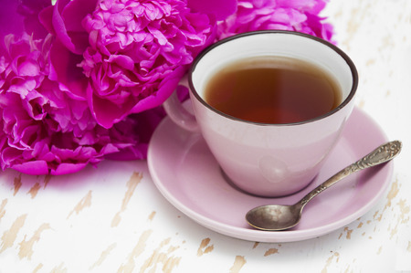 A cup of tea with flowers peonies on a wooden backgroundの写真素材